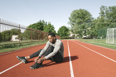 Sportsman sitting on racetrack and tying shoes before workout - AHSF00430