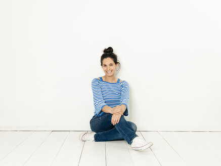 Beautiful young woman with black hair and blue white striped sweater sitting on the ground in front of white background - HMEF00419