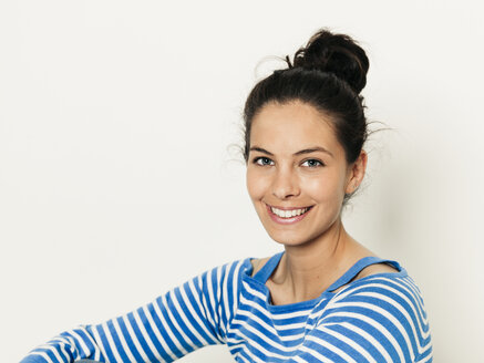 Schöne junge Frau mit schwarzen Haaren und blau-weiß gestreiften Pullover ist vor dem weißen Hintergrund posiert - HMEF00425