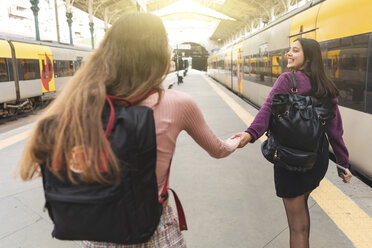 Rückenansicht von zwei jungen Frauen mit Rucksäcken Hand in Hand auf dem Bahnsteig, Porto, Portugal - WPEF01557