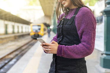 Junge Frau steht auf einem Bahnsteig und benutzt ein Smartphone, Porto, Portugal - WPEF01558