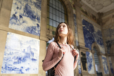 Young woman with backpack standing in front of station building looking around, Porto, Portugal - WPEF01562