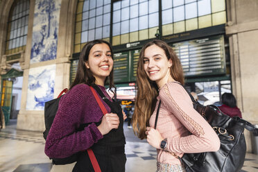 Porträt von zwei lächelnden jungen Frauen mit Rucksäcken vor einem Bahnhofsgebäude, Porto, Portugal - WPEF01563