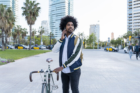 Lässiger Geschäftsmann mit Fahrrad auf Handy in der Stadt, Barcelona, Spanien, lizenzfreies Stockfoto