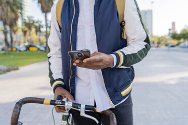 Nahaufnahme eines lässigen Geschäftsmannes mit Fahrrad, der ein Mobiltelefon in der Stadt benutzt, Barcelona, Spanien - AFVF03036
