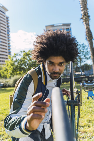 Lässiger Geschäftsmann, der ein Fahrrad in einem Stadtpark untersucht, Barcelona, Spanien, lizenzfreies Stockfoto