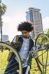 Lässiger Geschäftsmann mit Mobiltelefon und Fahrrad in einem Stadtpark, Barcelona, Spanien - AFVF03053