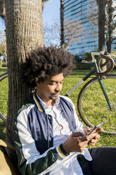 Lässiger Geschäftsmann mit Fahrrad und Mobiltelefon in einem Stadtpark, Barcelona, Spanien - AFVF03058