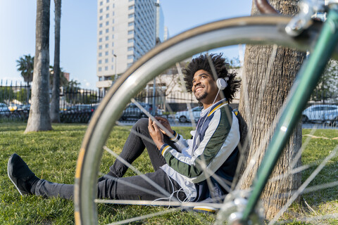 Lässiger Geschäftsmann mit Fahrrad, der in einem Stadtpark eine Pause einlegt und Musik hört, Barcelona, Spanien, lizenzfreies Stockfoto