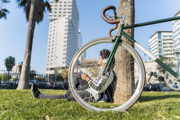 Casual businessman with bicycle taking a break in urban park listening to music, Barcelona, Spain - AFVF03067