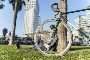 Lässiger Geschäftsmann mit Fahrrad, der in einem Stadtpark eine Pause einlegt und Musik hört, Barcelona, Spanien - AFVF03067