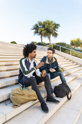 Two casual businessmen sitting on stairs having lunch break - AFVF03110