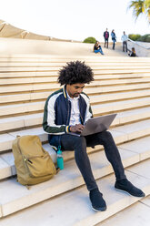 Casual businessman sitting on stairs working on laptop - AFVF03119