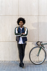 Porträt eines lächelnden lässigen Geschäftsmannes mit Fahrrad an einer Wand stehend - AFVF03130