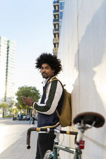 Casual businessman with bicycle and cell phone in the city, Barcelona, Spain - AFVF03137