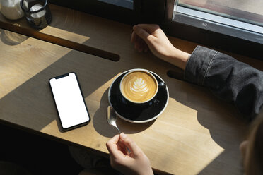 Junge Frau mit Tasse Kaffee und Smartphone in einem Café - FBAF00630