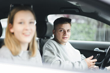 Portrait of young man with smartphone at driver's seat - FBAF00639