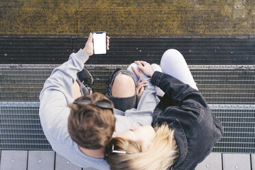 Junges Paar sitzt auf einer Treppe und schaut auf ein Smartphone - FBAF00651