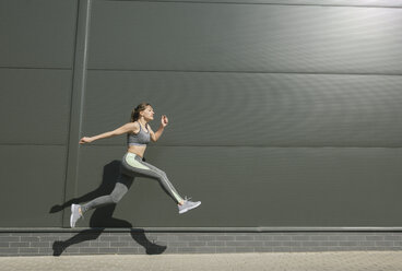 Sportlerin springt vor einer grauen Wand - AHSF00443