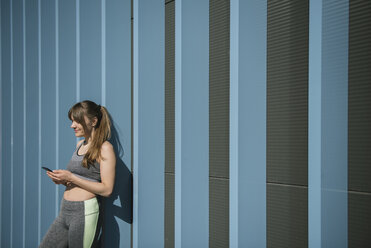 Sportswoman using phone in front of blue wall - AHSF00446