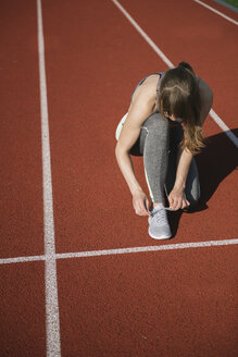 Sportswoman on racetrack tying shoes - AHSF00459