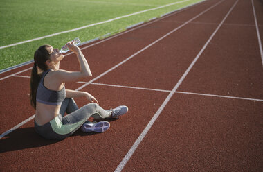 Sportlerin sitzt auf der Rennbahn und trinkt Wasser nach dem Training - AHSF00466