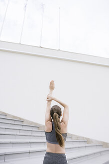 Rear view of woman raising arm, stretching on concrete bleachers - AHSF00482