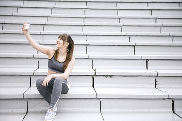 Junge Frau in Sportkleidung sitzt auf Beton Tribüne und macht Selfie - AHSF00486