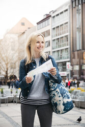Porträt einer lächelnden blonden Frau mit Karte und Gepäck in der Stadt, München, Deutschland - HMEF00429