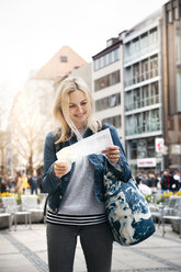 Porträt einer lächelnden blonden Frau mit Gepäck, die auf einen Stadtplan schaut, München, Deutschland - HMEF00430