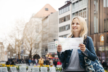 Porträt einer lächelnden blonden Frau mit Karte und Gepäck in der Stadt, München, Deutschland - HMEF00431