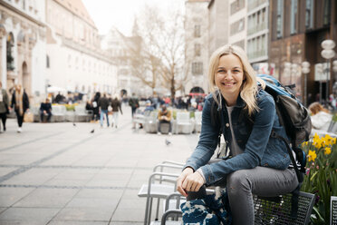 Portrait of smiling blond woman with baggage in the city, Munich, Germany - HMEF00432