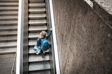 Woman with backpack and travelling bag standing on escalator looking around - HMEF00433