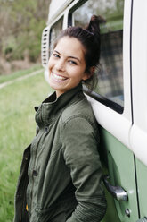 Lachende junge Frau, die sich an ein Wohnmobil lehnt - HMEF00451