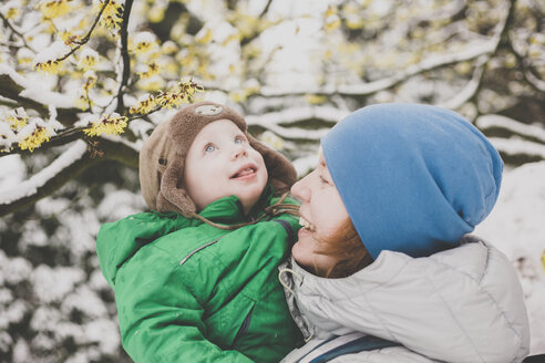 Porträt eines kleinen Jungen, der seinen ersten Schnee in den Armen seiner Mutter genießt - IHF00078