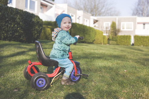 Porträt eines glücklichen kleinen Jungen mit Dreirad auf dem Rasen - IHF00087
