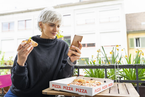 Frau isst Pizza in einer Pizzeria und benutzt ihr Smartphone, lizenzfreies Stockfoto