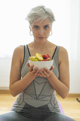 Frau, die zu Hause Yoga praktiziert und einen gesunden Obstsnack zu sich nimmt - FBAF00680