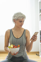 Woman practising yoga at home, having a healthy fruit snack - FBAF00682