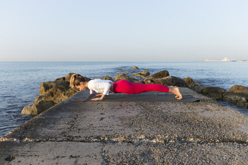 Young woman practicing yoga on the beach, doing chaturanga dhandasana - JPTF00092