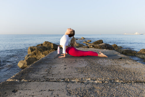 Young woman practicing yoga on the beach, doing cobra pose - JPTF00093