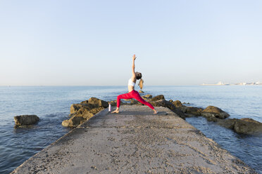 Junge Frau, die am Strand Yoga übt und die Kriegerpose einnimmt - JPTF00097