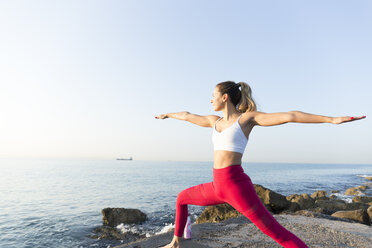 Junge Frau, die am Strand Yoga übt und die Kriegerpose einnimmt - JPTF00098