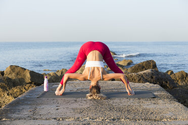 Young woman practicing yoga on the beach, doing prasarita padottanasana - JPTF00099