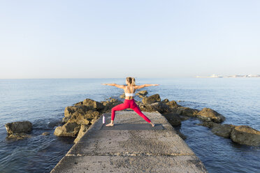 Junge Frau, die am Strand Yoga übt und die Kriegerpose einnimmt - JPTF00100