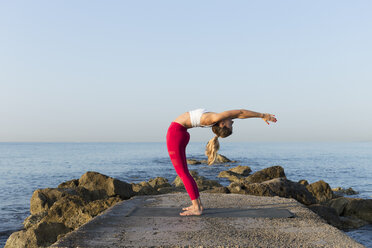 Junge Frau, die am Strand Yoga übt und einen Hintergrund macht - JPTF00103