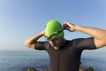 Triathlet bereitet sich auf das Schwimmen vor, setzt Badekappe und Schwimmbrille auf - JPTF00106