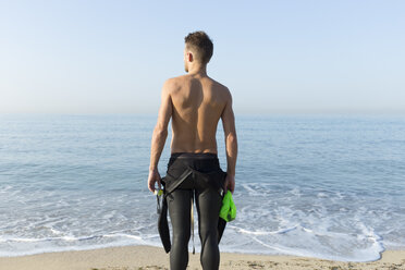 Rückansicht eines jungen Sportlers am Strand, der sich auf das Schwimmen vorbereitet - JPTF00112