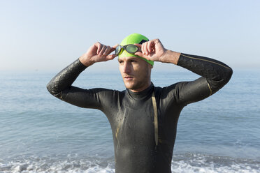 Triathlet bereitet sich auf das Schwimmen vor, setzt Badekappe und Schwimmbrille auf - JPTF00120