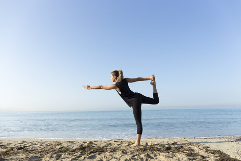 Young woman practicing yoga on the beach, doing dancer pose - JPTF00121